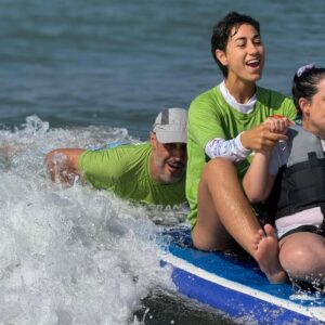 Teresa con síndrome de Rett en la jornada Onades Inclusives de SUPerando, disfrutando de una ola junto a dos voluntarios de SUPerando