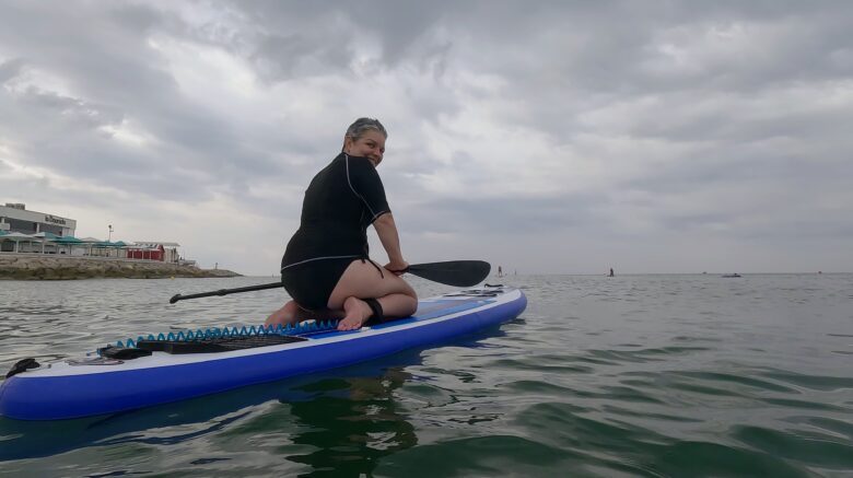 Mujer practicando paddle surf inclusivo adaptado en el mar dentro del proyecto Remando la vida de SUPerando para mujeres con cáncer de mama